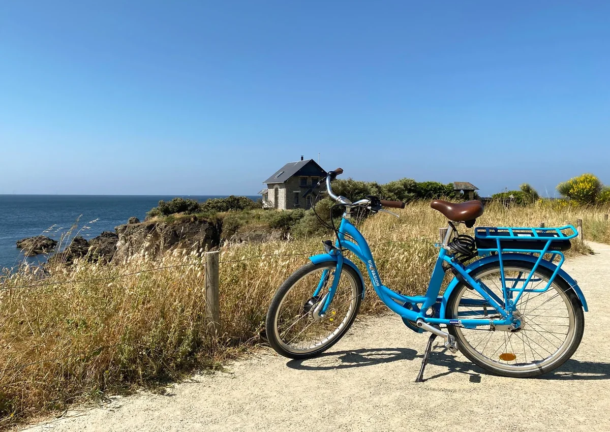 Vélo électrique bleu Bikevasion stationné au bord du sentier côtier face à l'océan