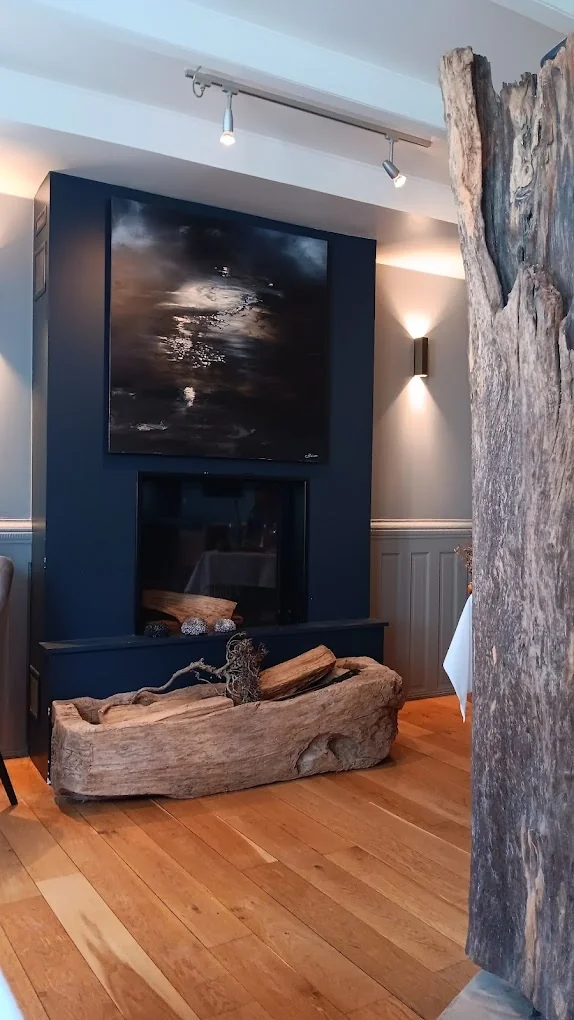 Cheminée habillée d'un grand tableau marin sombre et tronc en bois flotté au restaurant brut.