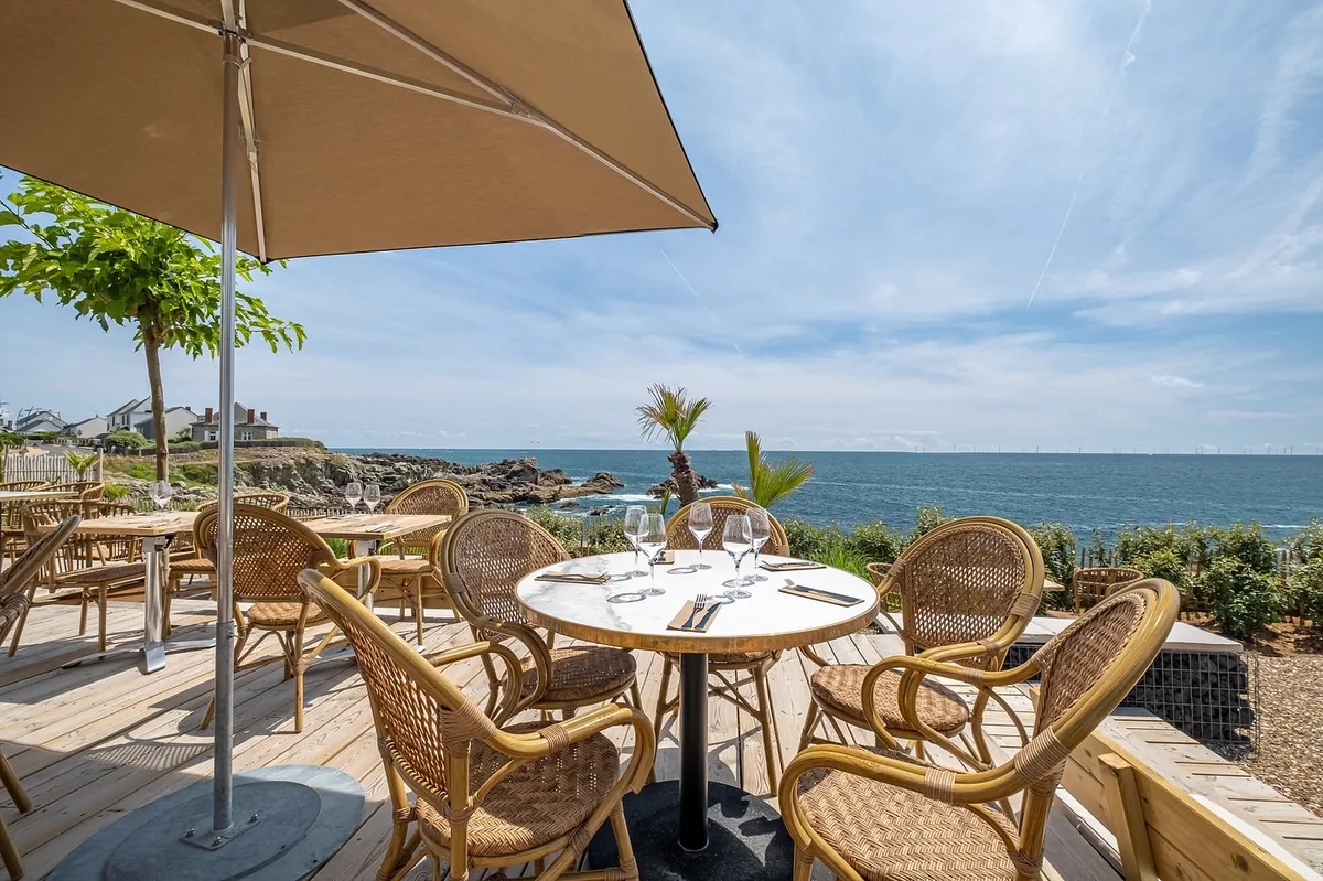 Terrasse extérieure du restaurant Coco à Batz-sur-Mer en bord d'océan, fauteuils en rotin et parasols beiges
