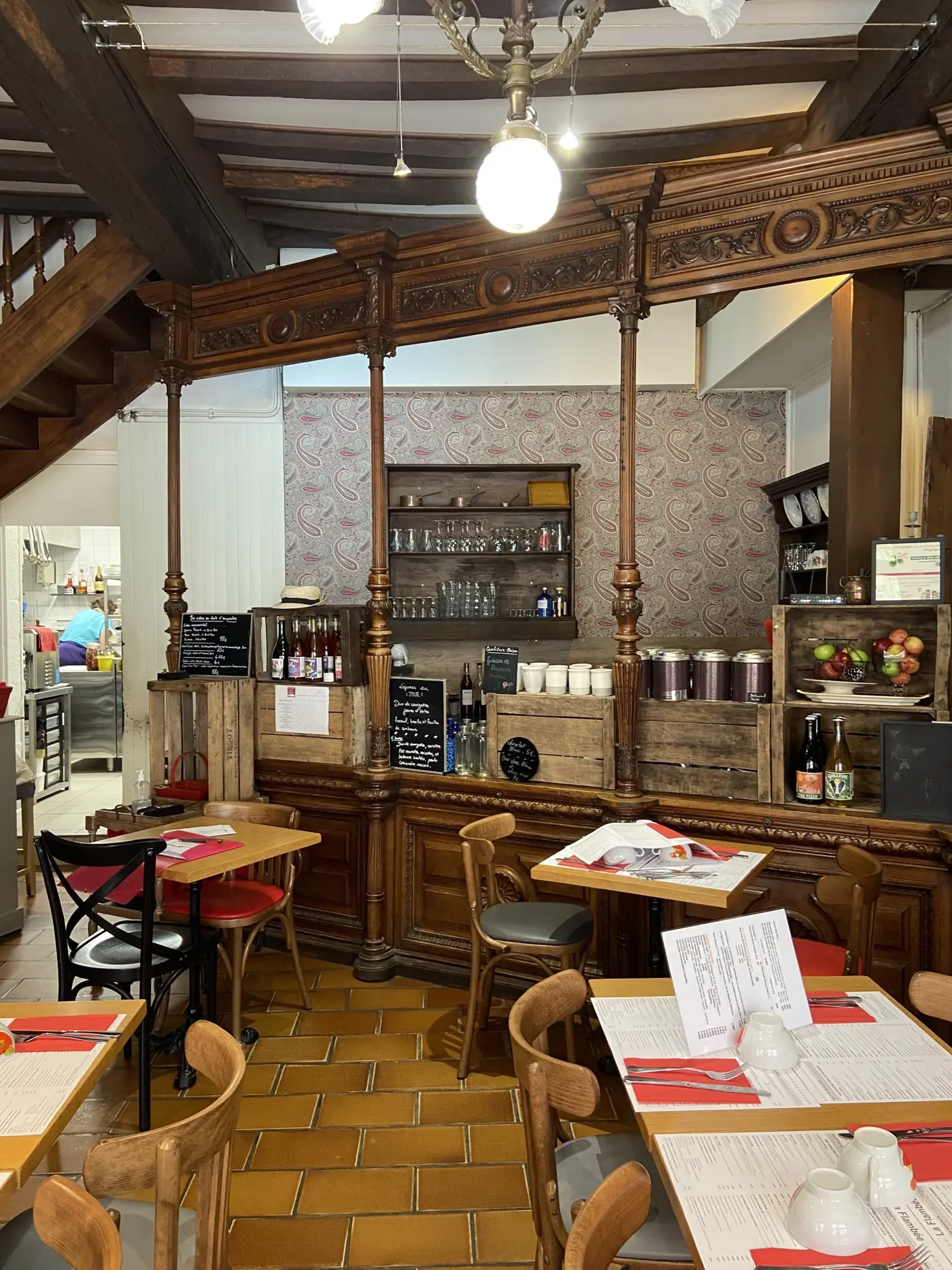 Intérieur chaleureux de La Flambée à Guérande avec comptoir bistrot en bois sculpté, étagères de bocaux et cuisine ouverte