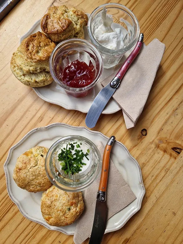 Assiettes de scones nature et au fromage frais accompagnés de confiture rouge et de crème, couteaux Laguiole
