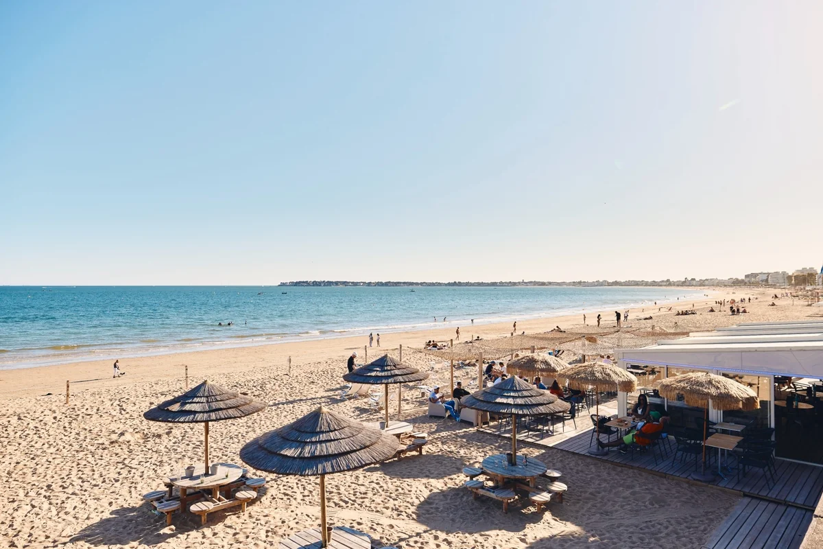 Restaurant de plage avec parasols en paille sur le sable de La Baule, baigneurs et vue sur la baie
