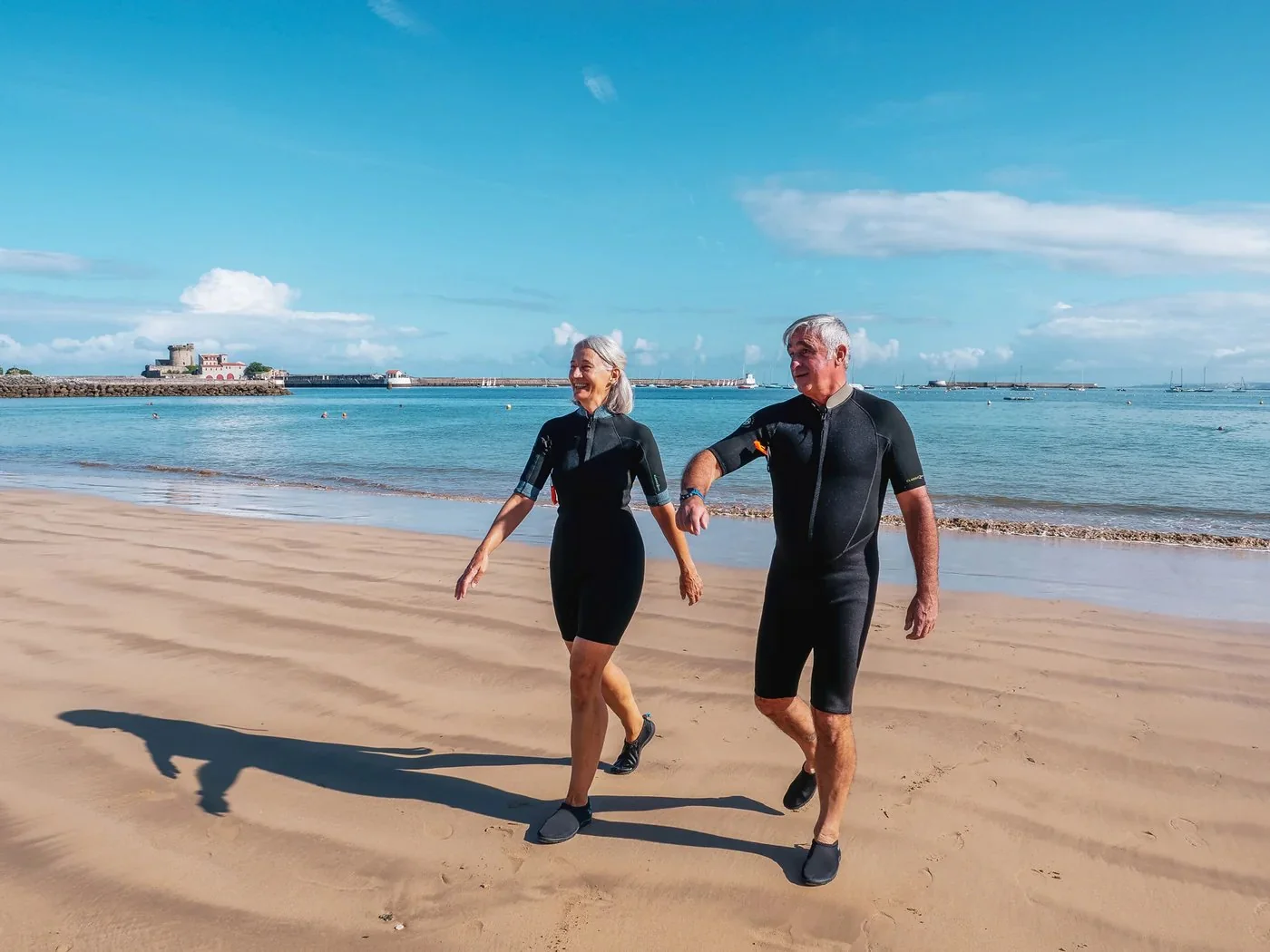 Couple en combinaison néoprène marchant sur la plage après une séance de longe-côte