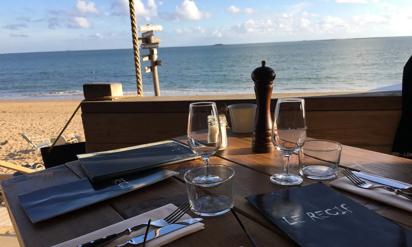 Table dressée Le Récif avec verres gravés et menu ardoise face à la mer au coucher de soleil