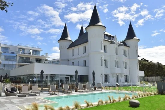 Façade du Château des Tourelles à Pornichet avec piscine extérieure, transats et pelouse